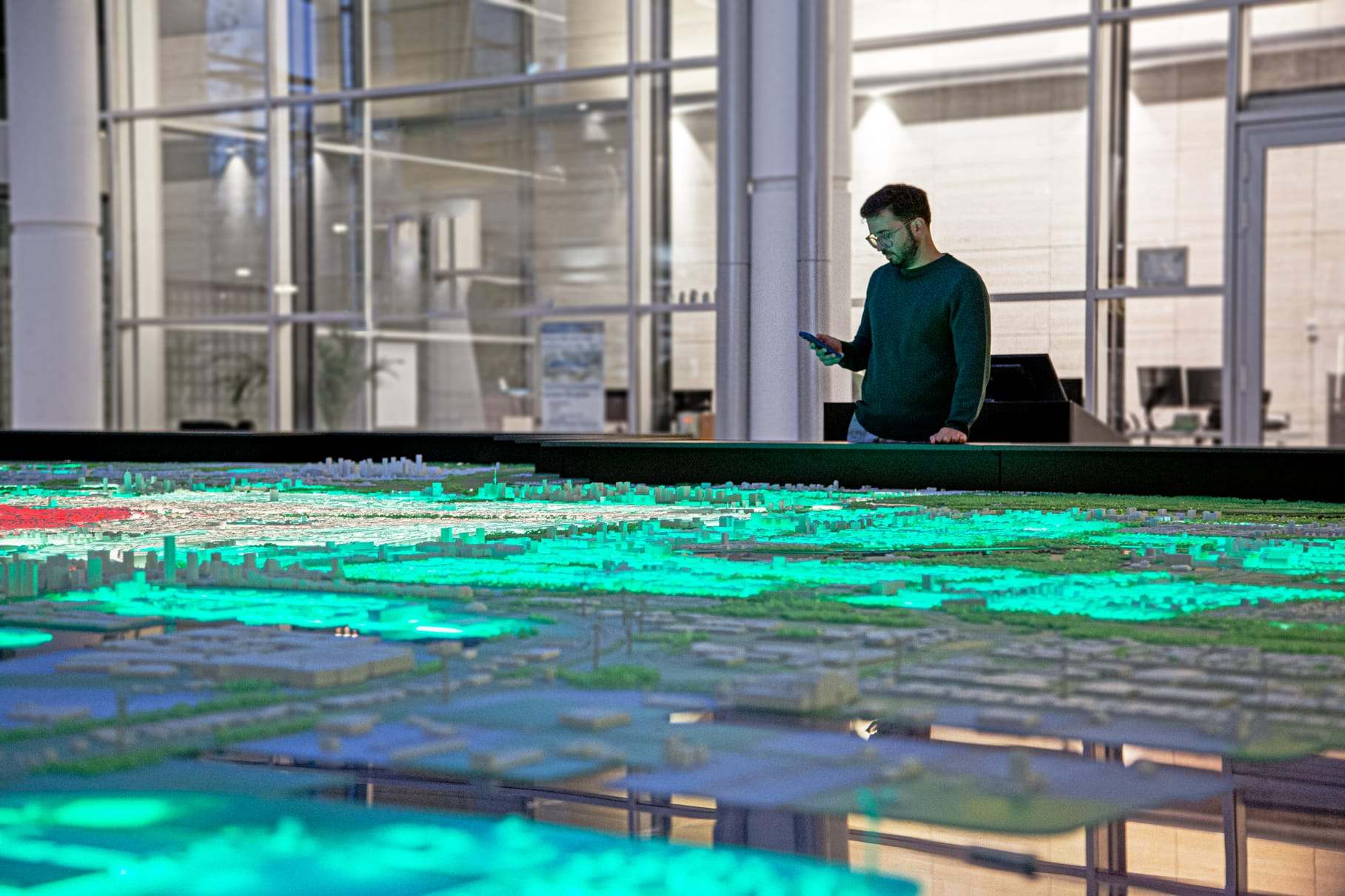 A visitor beside the city model, the surface lit in turquoise