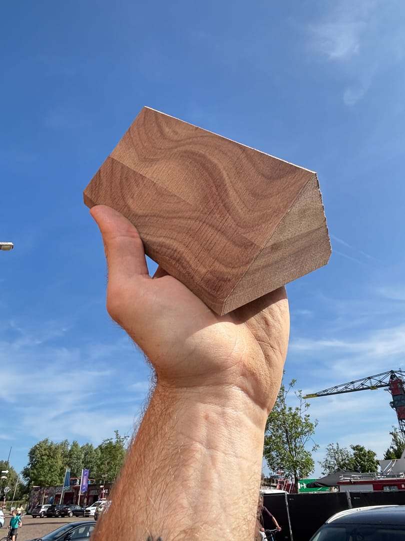 A hand holding up a block of walnut wood against a blue sky