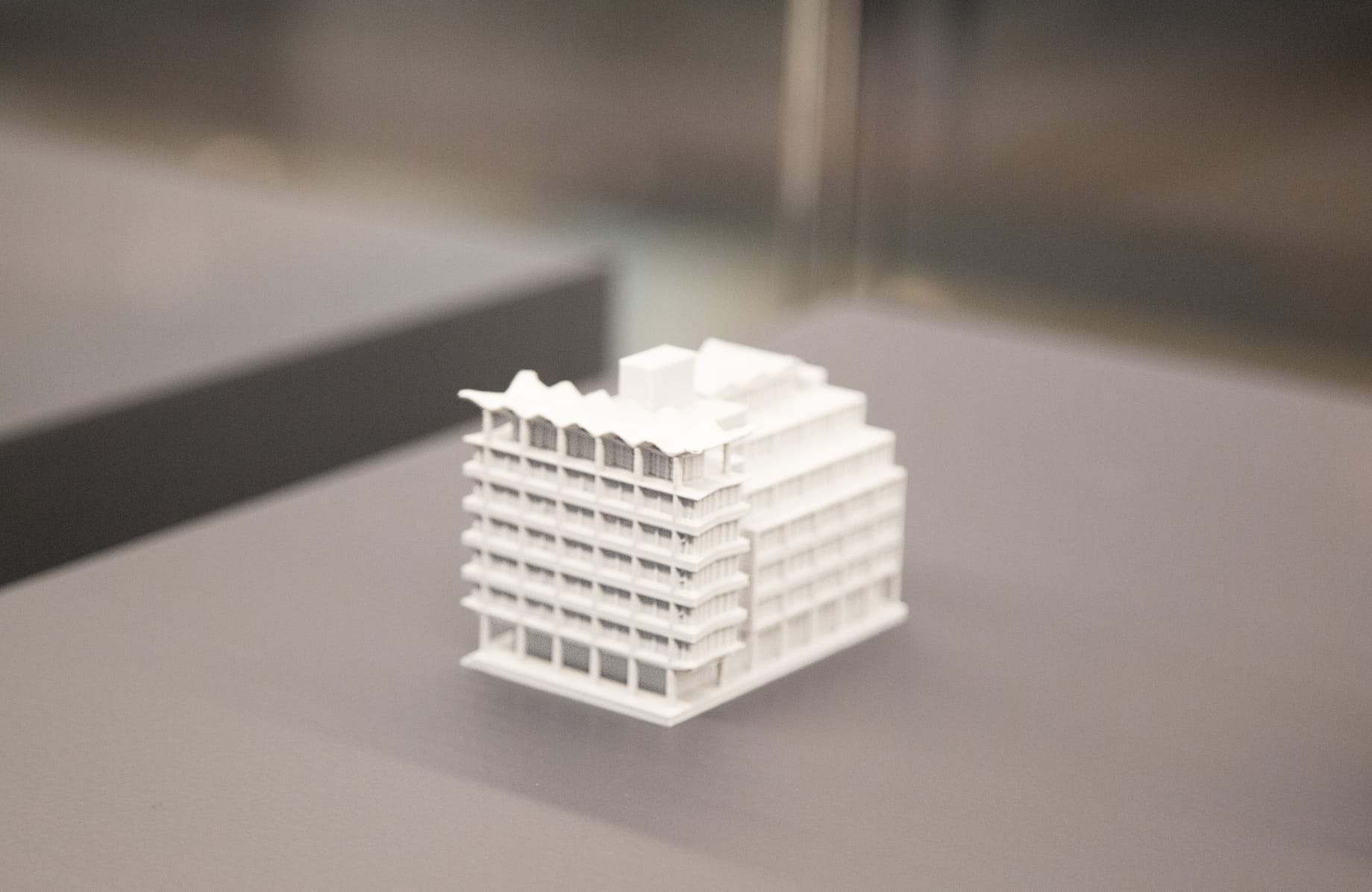 A small white 3D-printed model of an office block in a display case