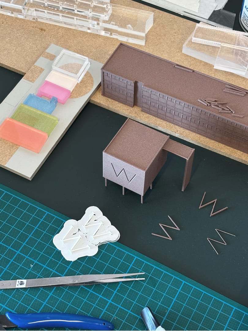 The workshop table with cut card shapes, the W lettering and a cutting mat