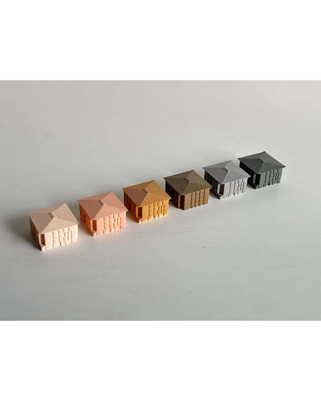 Six small 3D-printed house models in colours from pink to dark grey