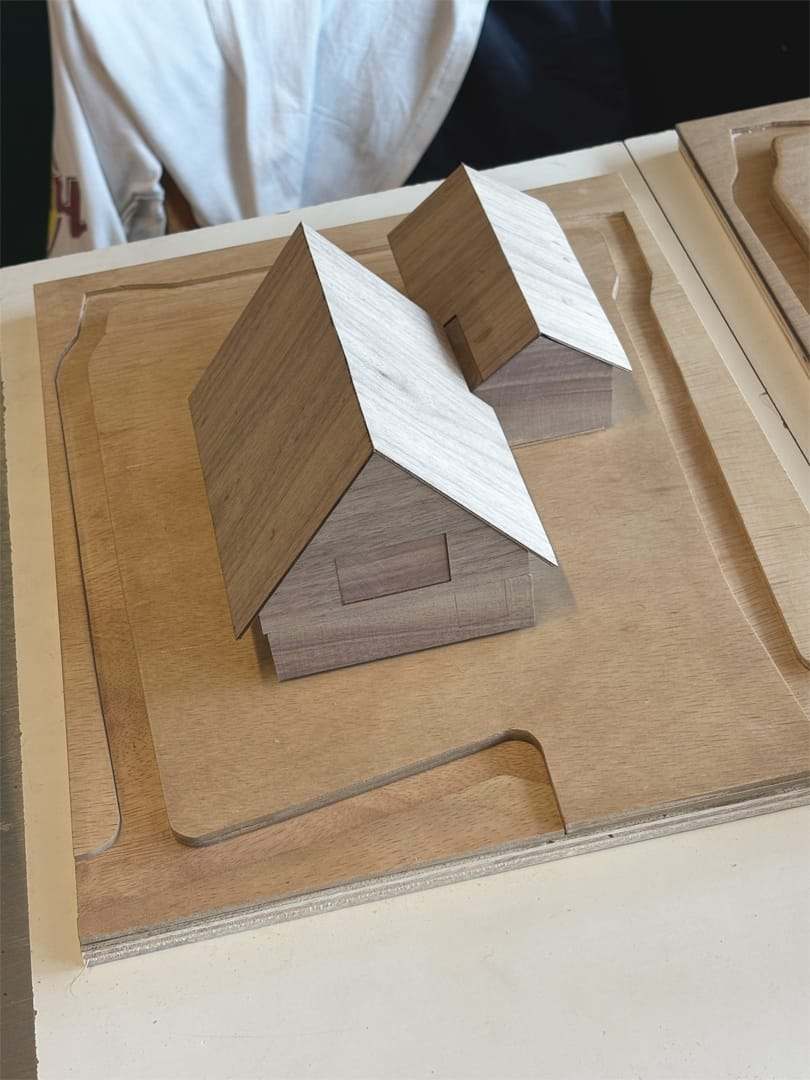 Two walnut volumes with pitched roofs on a plywood site base, held in front of a person