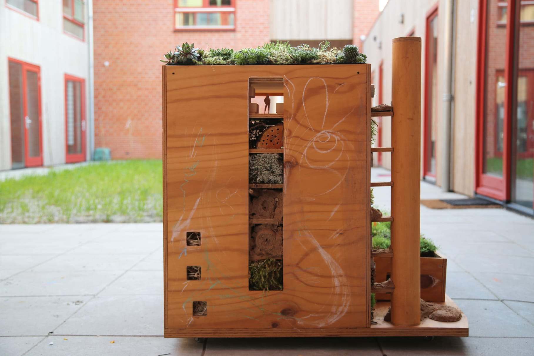 The insect hotel against the brick facade, with the drawing still on the plywood