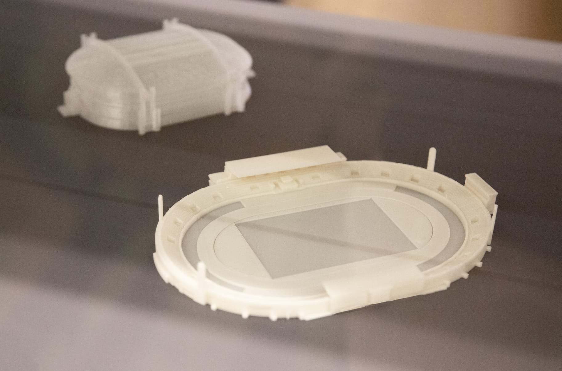 A white 3D-printed stadium model in a display case